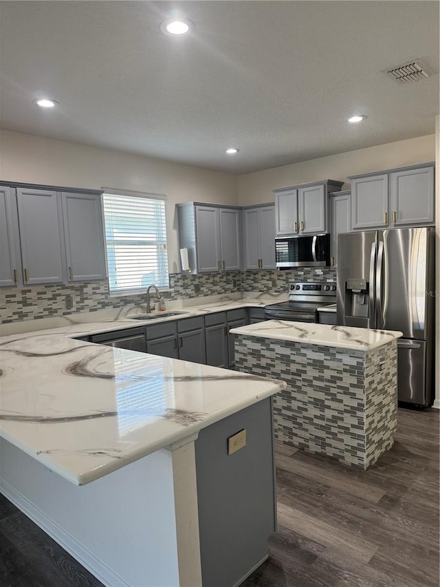 1954 Marabou Dr, Davenport, FL 33896 - kitchen with appliances with stainless steel finishes, gray cabinetry, a peninsula, tasteful backsplash, and light stone counters