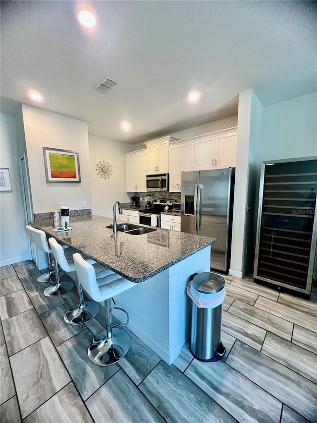 3191 Pequod Pl, Kissimmee, FL 34746 - kitchen with appliances with stainless steel finishes, beverage cooler, dark stone countertops, white cabinetry, and a breakfast bar area