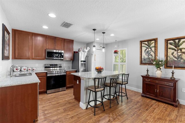 43 Pergola Pl, Ormond Beach, FL 32174 - kitchen with appliances with stainless steel finishes, a breakfast bar area, light wood-style flooring, a kitchen island, and a textured ceiling