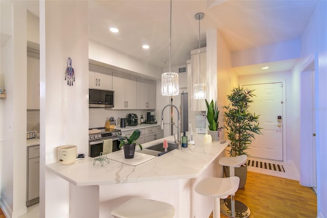 5554 Metrowest Blvd Unit 305, Orlando, FL 32811 - kitchen featuring a kitchen breakfast bar, stainless steel appliances, a peninsula, decorative light fixtures, and light wood-style flooring