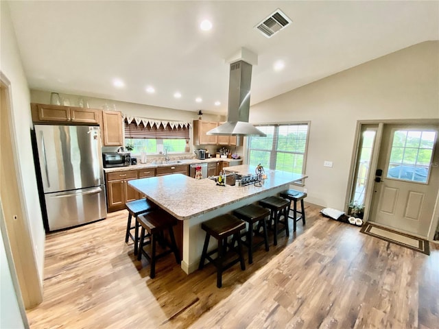 kitchen with light hardwood / wood-style floors, vaulted ceiling, appliances with stainless steel finishes, and island exhaust hood