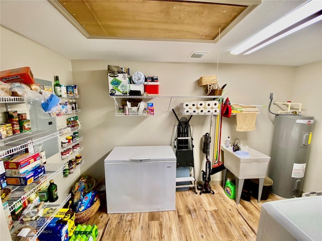 laundry room featuring water heater, sink, and light hardwood / wood-style flooring