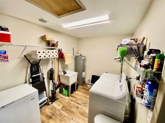 storage area featuring electric water heater, sink, and washer and clothes dryer