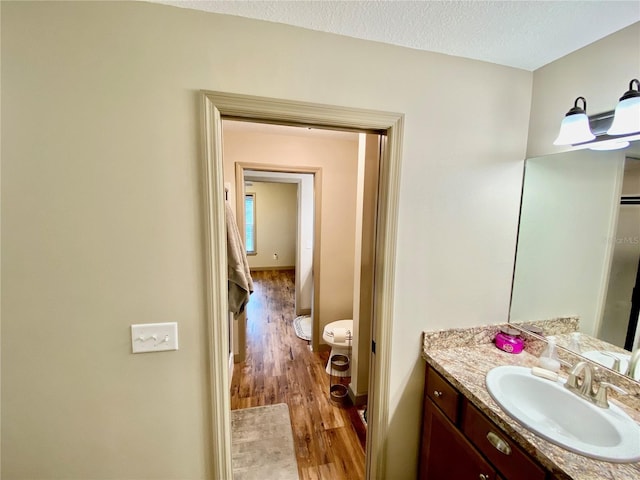 bathroom with a textured ceiling, vanity, toilet, and wood-type flooring