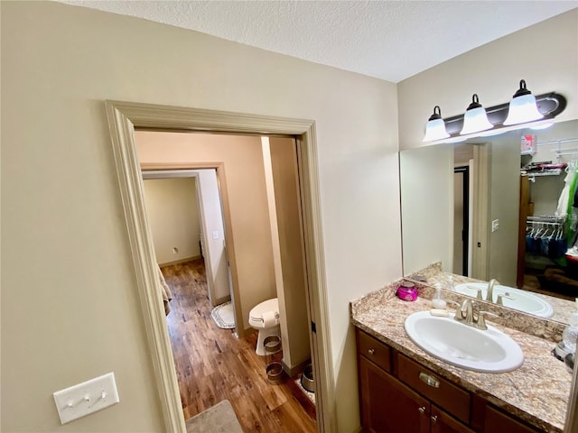 bathroom with toilet, a textured ceiling, vanity with extensive cabinet space, and hardwood / wood-style flooring