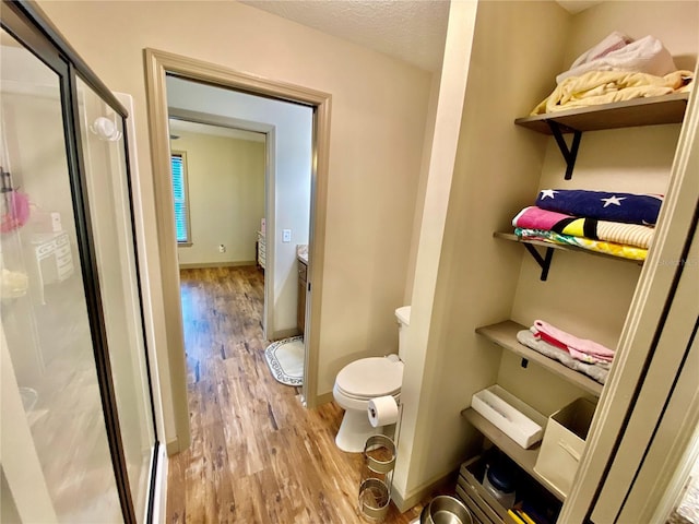 bathroom featuring a shower with door, a textured ceiling, wood-type flooring, and toilet