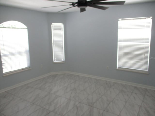 empty room with light tile flooring, ceiling fan, and a wealth of natural light