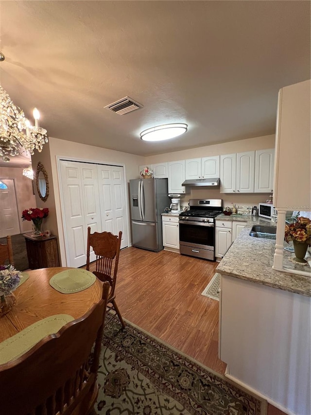 kitchen with white cabinetry, light stone counters, pendant lighting, stainless steel appliances, and light hardwood / wood-style floors