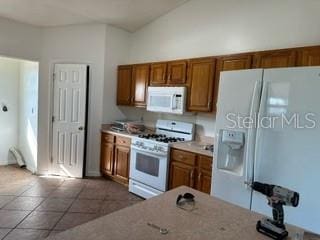 kitchen featuring dark tile flooring, white appliances, and vaulted ceiling