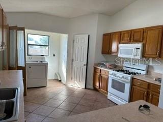 kitchen featuring white appliances, vaulted ceiling, washer / dryer, sink, and light tile floors