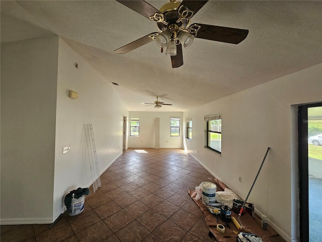 tiled empty room featuring lofted ceiling, ceiling fan, and a textured ceiling