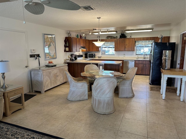 kitchen with hanging light fixtures, stainless steel appliances, a textured ceiling, and light tile floors