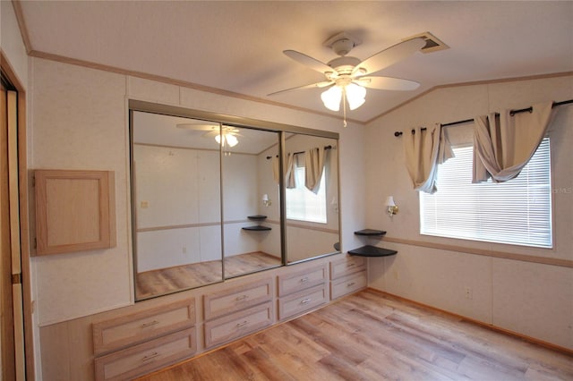 unfurnished bedroom with ceiling fan, crown molding, lofted ceiling, a closet, and light wood-type flooring