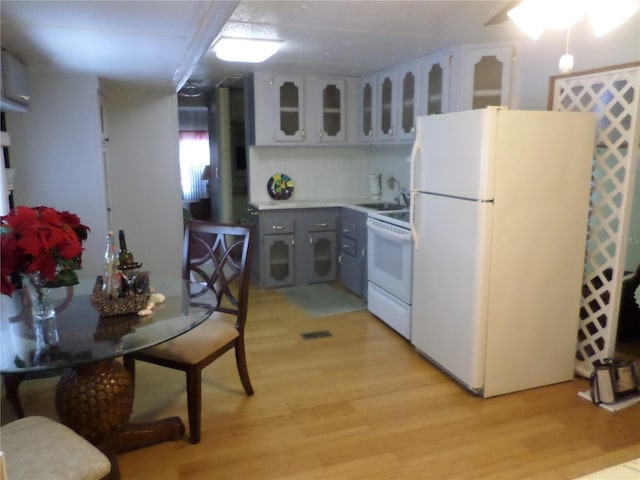 kitchen with white fridge, gray cabinetry, stove, sink, and light wood-type flooring