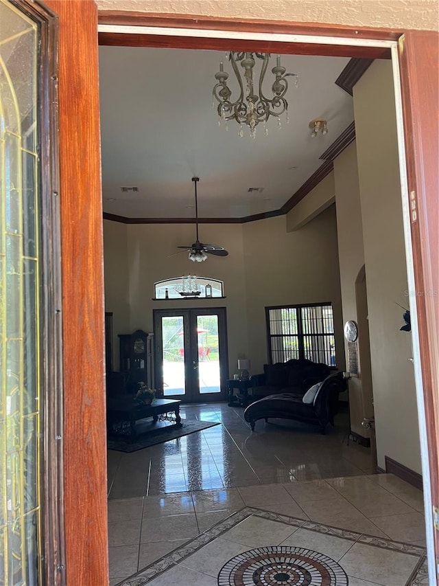 tiled living room with french doors, ceiling fan with notable chandelier, and ornamental molding