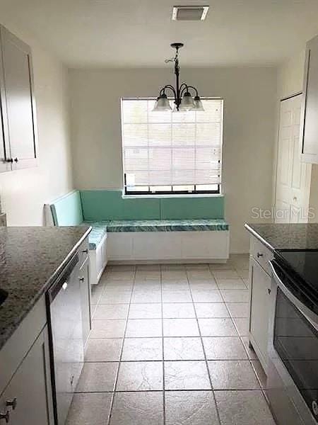 kitchen featuring pendant lighting, white cabinets, light tile patterned floors, appliances with stainless steel finishes, and a notable chandelier