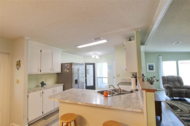 kitchen with white cabinetry, stainless steel fridge, sink, and kitchen peninsula