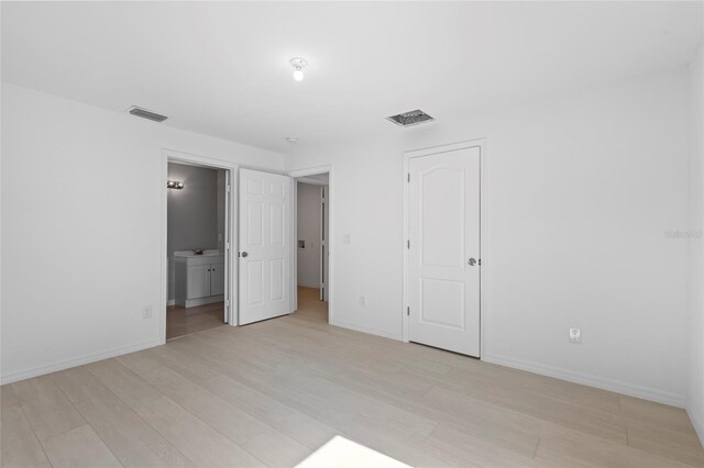 unfurnished bedroom featuring light hardwood / wood-style floors, sink, ensuite bathroom, and a closet