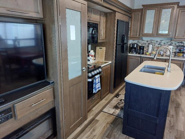 kitchen featuring sink, an island with sink, decorative backsplash, black appliances, and light wood-type flooring