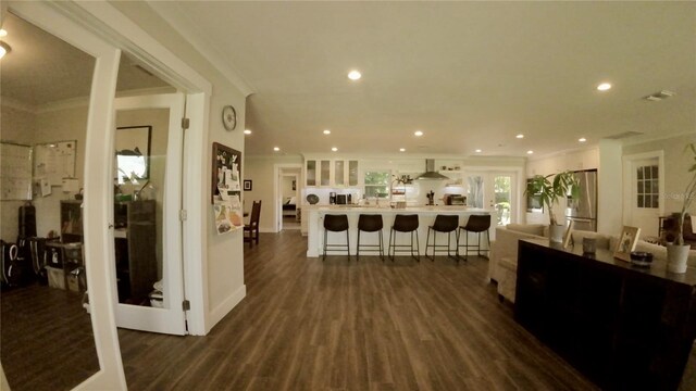 interior space with a breakfast bar area, wall chimney exhaust hood, dark wood-type flooring, ornamental molding, and stainless steel refrigerator