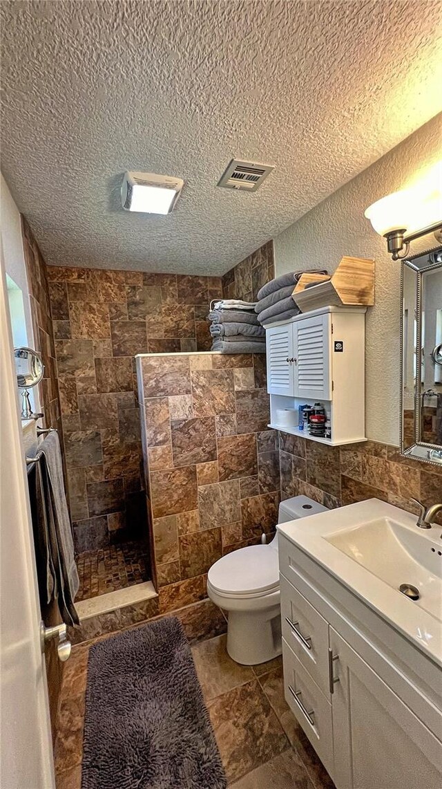 bathroom featuring tile walls, walk in shower, toilet, and vanity