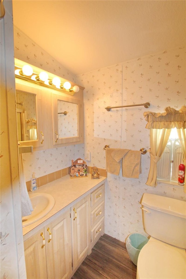 bathroom featuring toilet, wallpapered walls, wood finished floors, and vanity