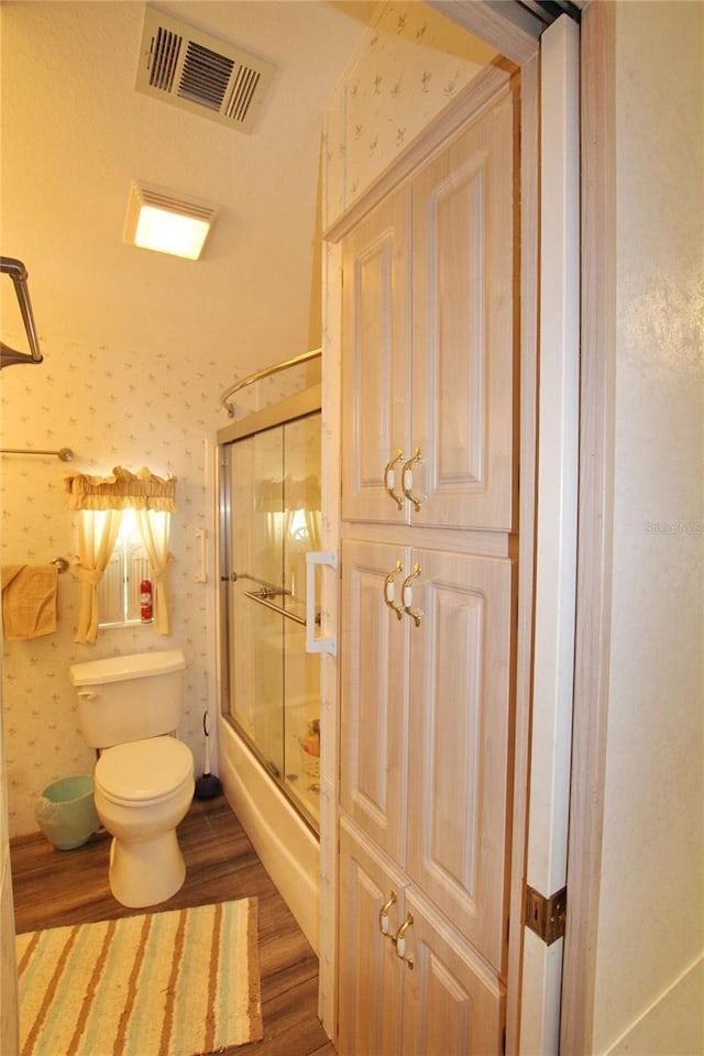 bathroom featuring visible vents, toilet, enclosed tub / shower combo, wood finished floors, and wallpapered walls