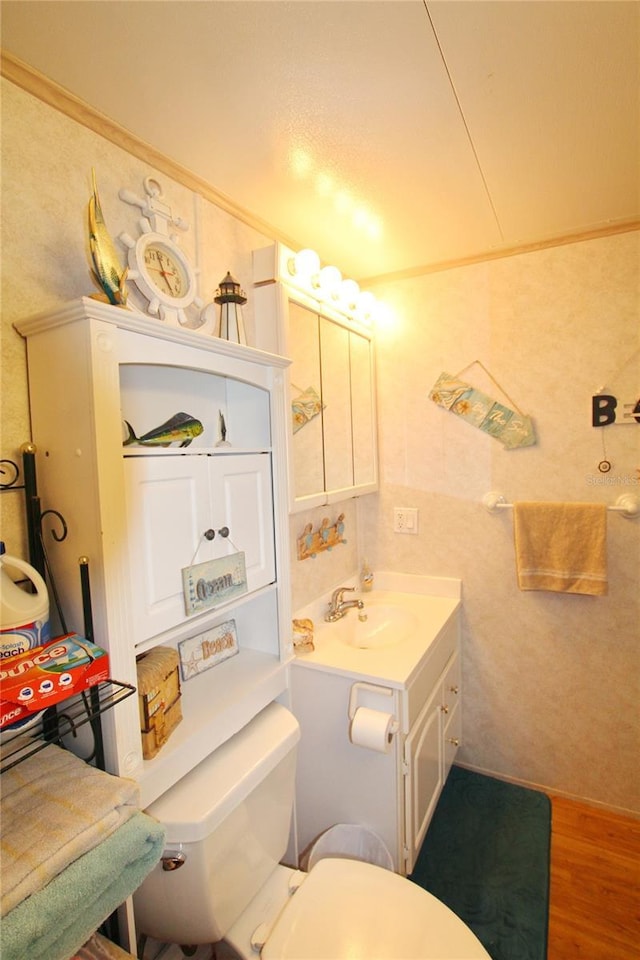 half bath with toilet, crown molding, wood finished floors, and vanity