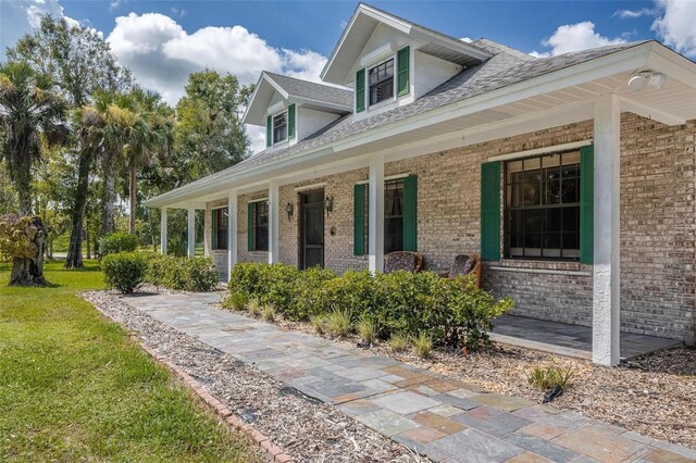 exterior space featuring a yard, covered porch, and brick siding