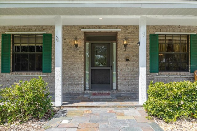 view of exterior entry with a porch and brick siding