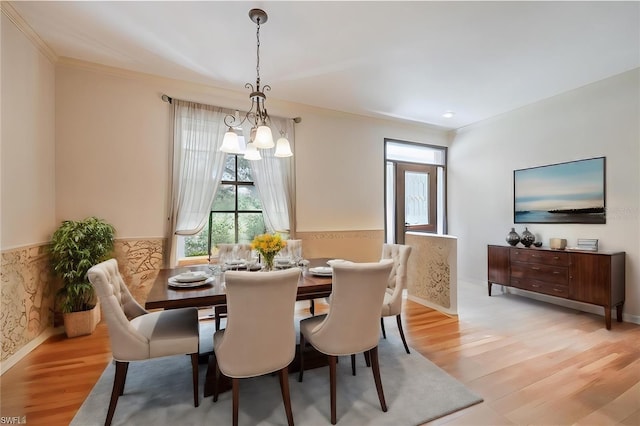 dining room featuring light wood-style flooring, ornamental molding, a wainscoted wall, and a chandelier