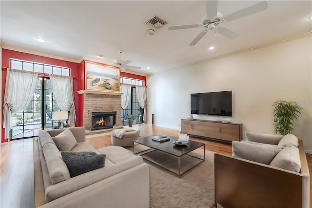 living room featuring ceiling fan, a fireplace, crown molding, and light hardwood / wood-style flooring