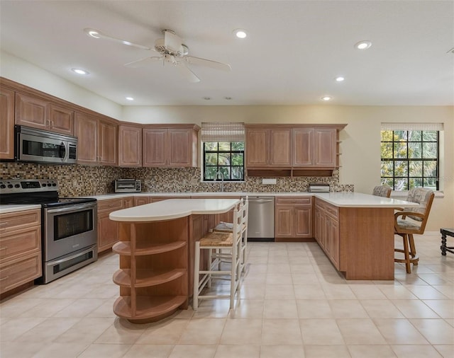 kitchen featuring open shelves, a peninsula, appliances with stainless steel finishes, a kitchen bar, and backsplash