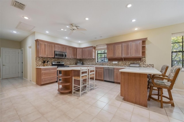 kitchen with tasteful backsplash, stainless steel appliances, kitchen peninsula, ceiling fan, and a breakfast bar area