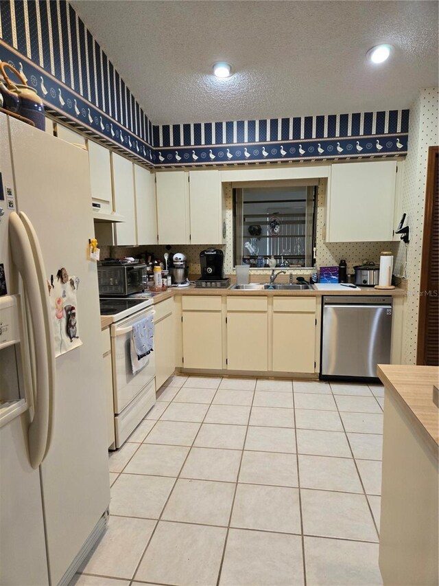 kitchen with sink, white appliances, cream cabinetry, and light tile patterned floors