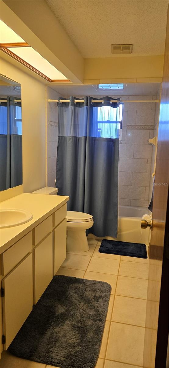 full bathroom featuring toilet, a textured ceiling, vanity, shower / bath combo, and tile patterned flooring