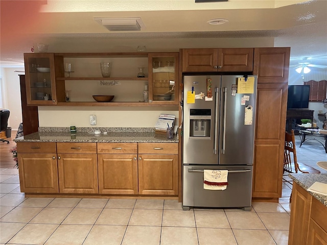 kitchen with dark stone countertops, light tile patterned flooring, ceiling fan, and stainless steel fridge with ice dispenser