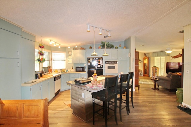 kitchen featuring light hardwood / wood-style flooring, black appliances, a breakfast bar area, and a textured ceiling