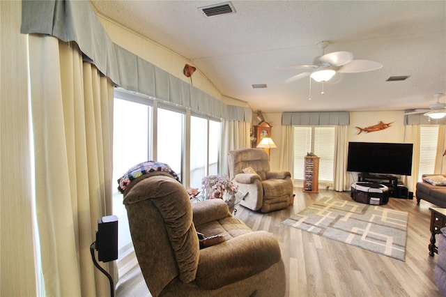 living room with ceiling fan, light hardwood / wood-style floors, a textured ceiling, and vaulted ceiling