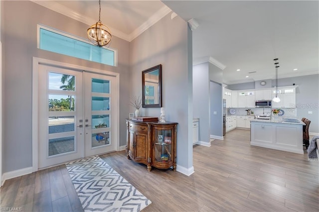 entryway with crown molding, french doors, light hardwood / wood-style flooring, and a notable chandelier