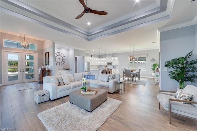 living room with crown molding, french doors, ceiling fan with notable chandelier, light hardwood / wood-style floors, and a raised ceiling