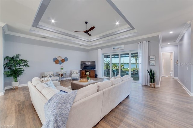 living room featuring a tray ceiling, crown molding, ceiling fan, and light hardwood / wood-style floors