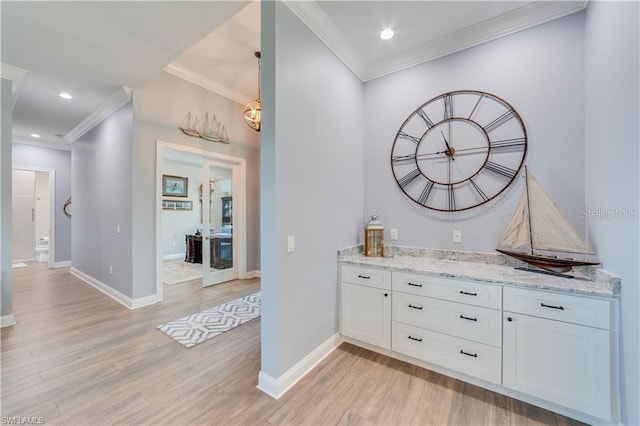 bar with white cabinets, decorative light fixtures, light stone countertops, light hardwood / wood-style floors, and ornamental molding