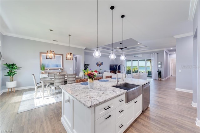 kitchen featuring light wood-type flooring, pendant lighting, a center island with sink, and white cabinets