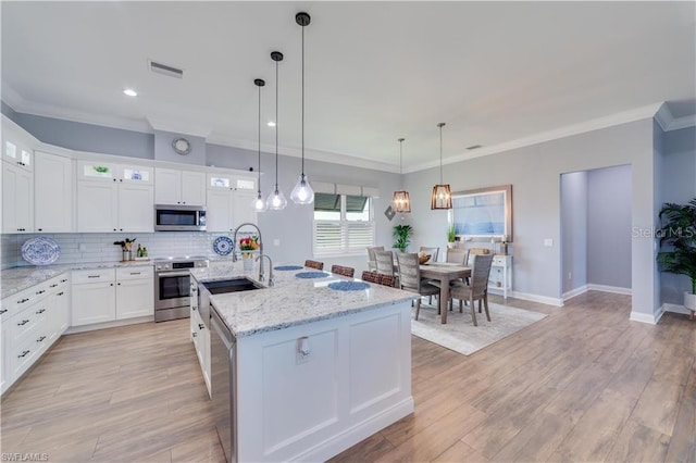 kitchen featuring a center island with sink, appliances with stainless steel finishes, hanging light fixtures, light wood-type flooring, and white cabinets