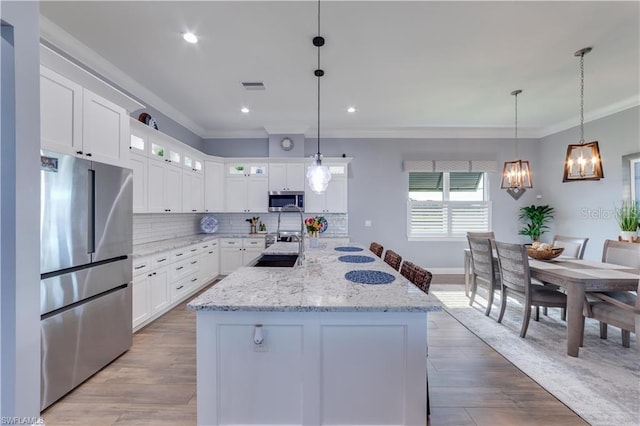 kitchen featuring light wood-type flooring, appliances with stainless steel finishes, white cabinets, and hanging light fixtures