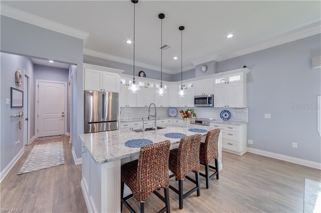 kitchen with light hardwood / wood-style flooring, an island with sink, sink, hanging light fixtures, and appliances with stainless steel finishes