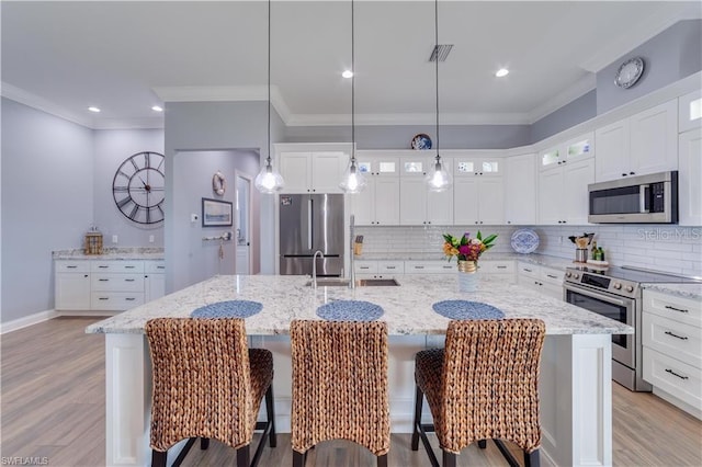 kitchen featuring a center island with sink, pendant lighting, appliances with stainless steel finishes, light stone counters, and light wood-type flooring