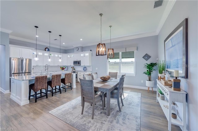 dining space featuring light hardwood / wood-style floors, crown molding, and sink