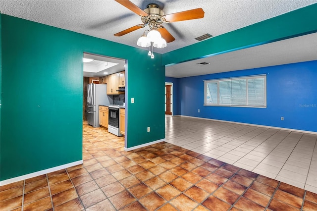 kitchen featuring tile patterned floors, stainless steel refrigerator, a textured ceiling, and white electric stove